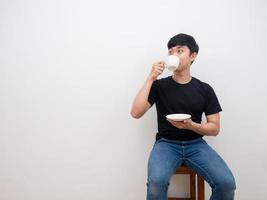 Handsome man drinking coffee cup in his hand and looking at space feel relax and sitting on chair on white background photo