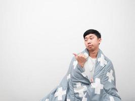 Asian man cover body by blanket and bored face point finger left side copy space on white background,Don't want to wake up concept photo