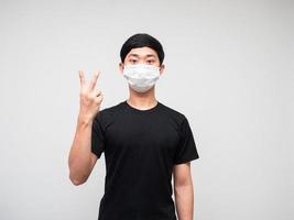 hombre asiático camisa negra con máscara muestra dos dedos contando sobre fondo blanco aislado foto