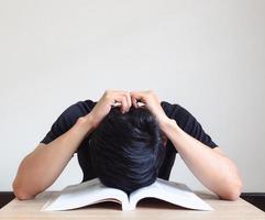 el hombre cierra la cabeza en un libro abierto y toca la cabeza con la mano en el escritorio siente foto