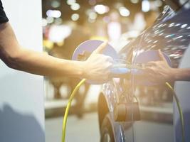 sujetar con la mano y con el pulgar hacia arriba el enchufe del vehículo de carga eléctrica y la luz de bengala para recargar la batería del coche energía de energía limpia de color negro para el concepto futuro foto