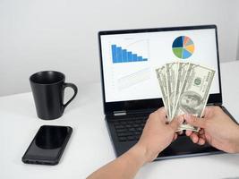 Man hand holding money dollar and using laptop on the table with mobile phone photo