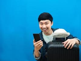 Man smiling hugging luggage with mobile phone blue background copy space photo