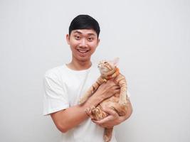 hombre asiático camisa blanca sonrisa feliz y alegre llevar gato naranja mira la cámara sobre fondo blanco foto