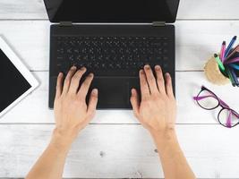 Hand on keypad of laptop with glasses and mobilephone on the table top view photo