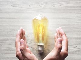 Hands protect yellow light bulb on wood table copy space,Inspiration business concept