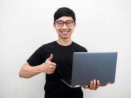 hombre asiático con gafas sosteniendo el pulgar del portátil hacia arriba y cara de sonrisa feliz sobre fondo blanco foto