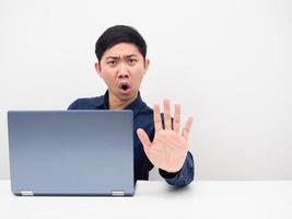 hombre con computadora portátil en la mesa muestra la mano para detener la cara enojada espacio de copia fondo blanco foto