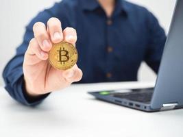 Close up man showing golden bitcoin on the table with laptop crop shot photo