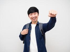 joven con mochila escolar cara sonriente y puño arriba portriat fondo blanco, hombre asiático con mochila concepto de regreso a la escuela foto