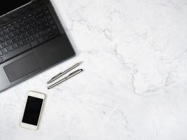 Laptop smartphone and silver pen on the marble table top view copy space photo