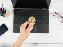 mano sujetando bitcoin en el teclado del fondo del portátil en el espacio de trabajo de la vista superior de la mesa foto