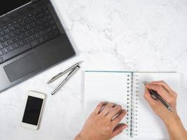 Top view workspace marble table hand writing on notebook with pen and mobile phone and laptop space photo