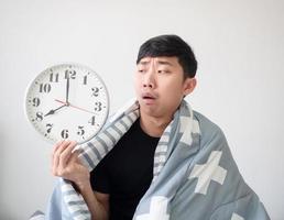 Asian man shocked face and looking at clock in hand and hug pillow on white isolated wake up late concept photo