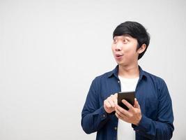 Asian young man holding and press mobile phone in his hand feeling excited and lookign at copy space white isolated photo