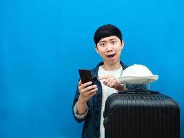 Man feeling amazed point at mobile phone with luggage blue background copy space photo