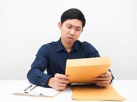 hombre asiático sentado en la mesa mirando el sobre de documentos en su mano sintiéndose aburrido foto