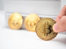 Closeup finger holding gold bitcoin on table with book background photo