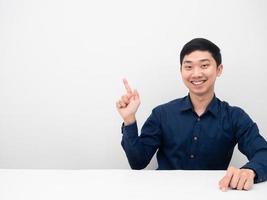 Cheerful man happy smile sitting and point finger at copy sapce white background photo