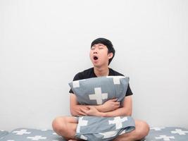 Asian man sit on the bed hug pillow feeling sleepy and yawn photo