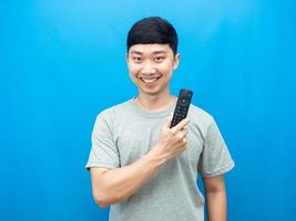 hombre asiático confiado sosteniendo televisión remota con un fondo azul sonriente foto