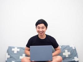 Cheerful man sitting on the bed with laptop white background photo