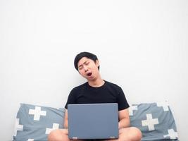 Man sit working with laptop on the bed feeling sleepy and yawn white background photo