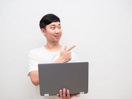 Asian man cheerful holding laptop point finger at space white background photo