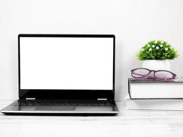 pantalla blanca del portátil en el escritorio con libro y gafas foto