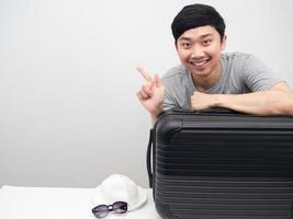 Asian man smiling with luggage point finger at copy space photo