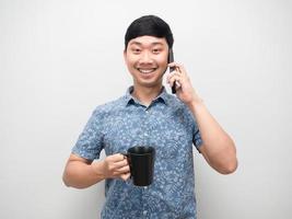 retrato, hombre asiático, camisa azul, tenencia, taza de café, y, teléfono móvil, sonriente, feliz foto