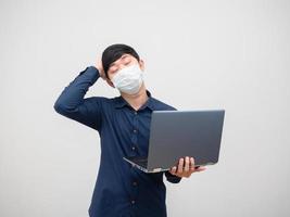 Sick man wearing mask feeling headache holding laptop in hand on white background photo