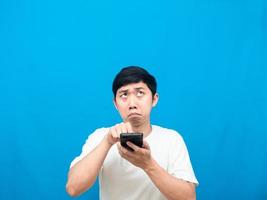 Asian man press at mobile phone in his hand felling afraid looking up at copy space blue background photo