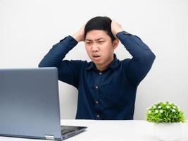 Man gesture strain and touch his head looking at laptopn on the table photo