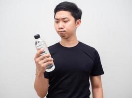 hombre asiático mirando una botella de agua en su mano y sintiendo dudas sobre fondo blanco foto