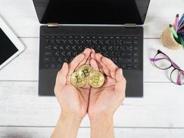 Hand holding gold bitcoins on the keyboard of laptop background on table top view workspace photo