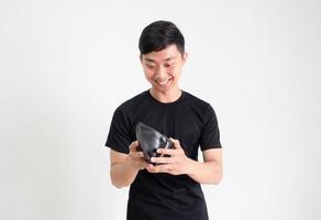 joven asiático camisa negra mira el dinero en efectivo en su billetera con una sonrisa y se siente feliz y en blanco aislado, concepto de hombre rico foto