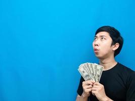 Man holding money feeling amazed looking at copy space blue background photo