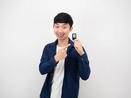 Handsome asian man point at car key in his hand with happy smile cheerful on white wall background photo