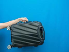 Man hand holding luggage on blue background holiday concept