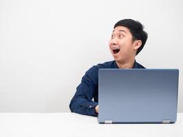 Man sitting with laptop on the table looking at copy space feeling amazed photo