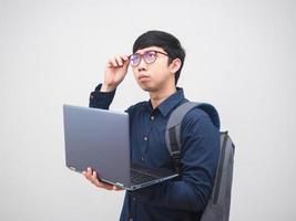 hombre de negocios asiático con mochila sosteniendo una laptop sintiéndose confundido tocuh sus glaases sobre fondo blanco foto