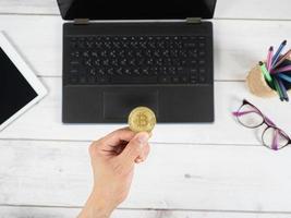 Hand holding gold bitcoin and mobilephone with laptop and tablet on wood table background photo