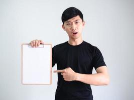 Young Asian man black shirt point finger at wood clipboard blank document in hand serious face on white isolated photo