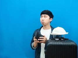 Man with luggage holding wallet feeling sad looking at copy space blue background photo