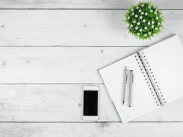 Workspace on white wood table top view copy space,Silver pen on blank page notebook and smartphome black screen photo