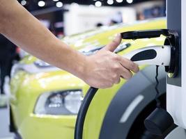 Toma de mano del vehículo de carga eléctrica para recargar la batería de la energía limpia del coche para el concepto futuro con un destello de luz foto