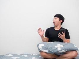 Asian man holding mobile phone on the bed feeling amazed looking at copy space photo