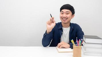 Man sit at the desk smiling and point pen at copy space photo