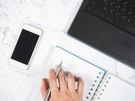 Workplace top view,Hand with pen on notebook smartphome and laptop on the table work from home concept photo